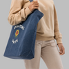Person holding a blue tote bag with a sunflower design and text on a white background